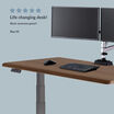 Five-star review graphic reading &ldquo;Life changing desk! Back soreness gone!!&rdquo; from Roy M., beside a close-up of a walnut electric standing desk with gray frame, control keypad, keyboard, mouse and dual monitor arm.